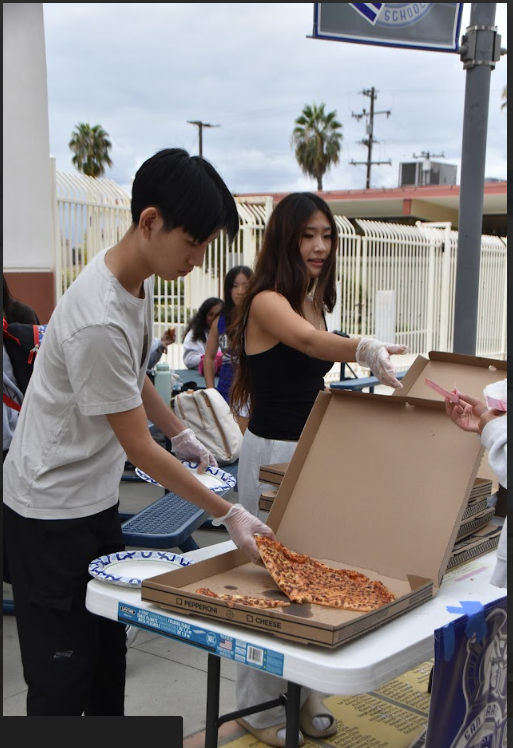 Sports and broadcast hands out pizza slices to eager customers.